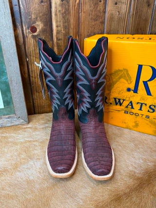 A pair of western cowboy boots with dark teal shafts featuring gray embroidered star patterns and burgundy crocodile-embossed toes, displayed on a tan hide rug with a yellow R.W.
