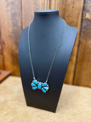 Necklace with blue floral pendant on a black stand against a wooden background