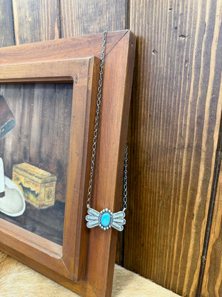 Necklace with a turquoise pendant hanging from a wooden frame.