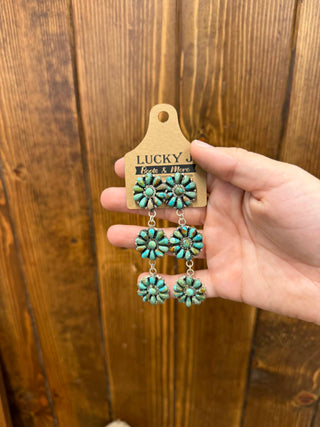 stamped Turquoise floral earrings on a wooden panel with 'Lucky' brand tag.