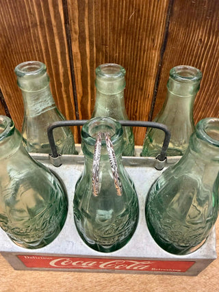 Set of vintage green Coca-Cola bottles holding a set of sterling silver hoop earrings in a metal holder against a wooden background