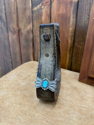 Decorative wooden block with a metal embellishment featuring a turquoise stone and silver flower design, against a wooden background.