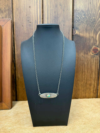 Silver necklace with a pendant on a black mannequin bust against a wooden background