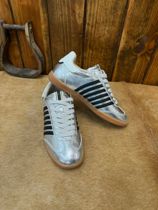 Pair of silver sneakers with black stripes on a wooden floor.