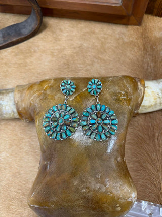 Turquoise earrings on a glass mannequin head with a wooden background