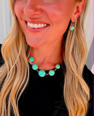 A close-up lifestyle shot of a woman wearing a turquoise and silver beaded necklace and matching drop earrings.
