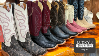 Row of cowboy boots displayed on a wooden shelf with Lucky J Boots & More branding.