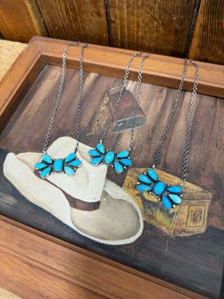 Necklace with blue floral design on a wooden surface with a cowboy boot and hat.
