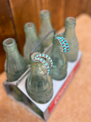 Set of green glass bottles with turquoise jewelry on a wooden surface