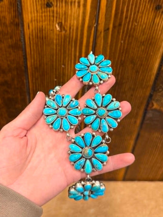 Turquoise flower-shaped earrings held in a hand against a wooden background